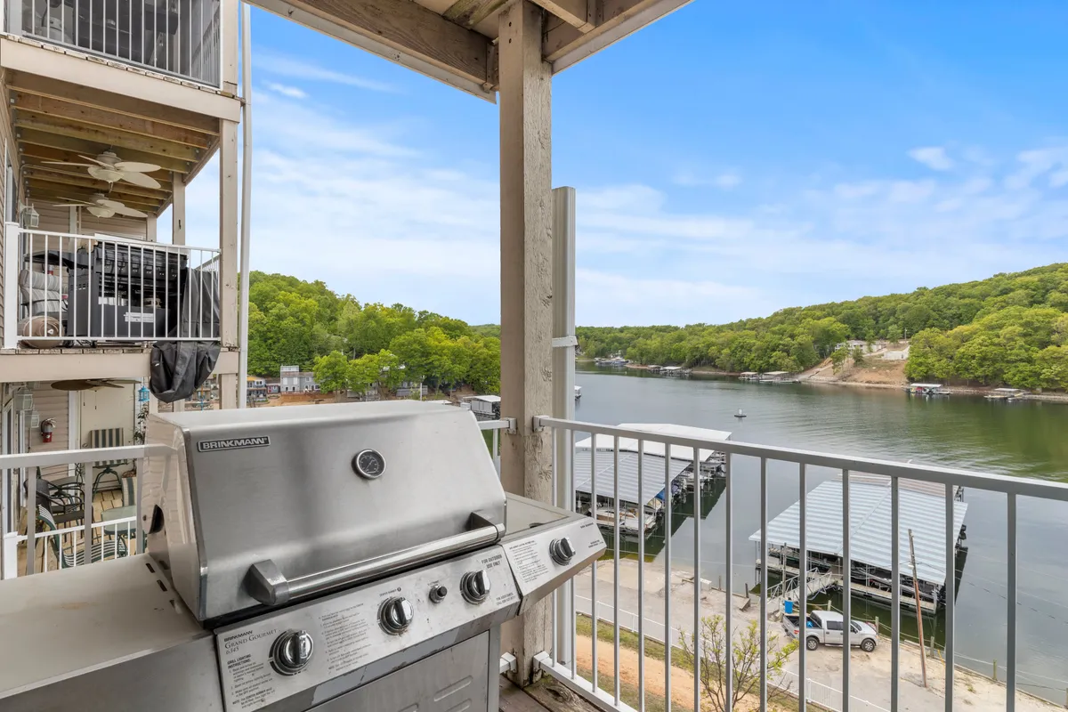 An exterior shot of a balcony with a grill and comfortable seating, overlooking the serene lake and lush green trees. The scene captures moments of outdoor cooking, social gatherings, and tranquil mornings by the water, highlighting the deck’s versatility for both quiet and lively occasions.