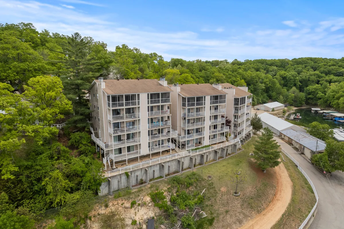 This image shows a three-story condo building nestled among lush greenery, with balconies furnished with chairs that invite relaxation. The natural surroundings are prominent, with tall trees and glimpses of the water beyond, suggesting proximity to nature and wildlife. The mood is serene and inviting, ideal for observing the area's fauna or simply soaking up the tranquil setting.