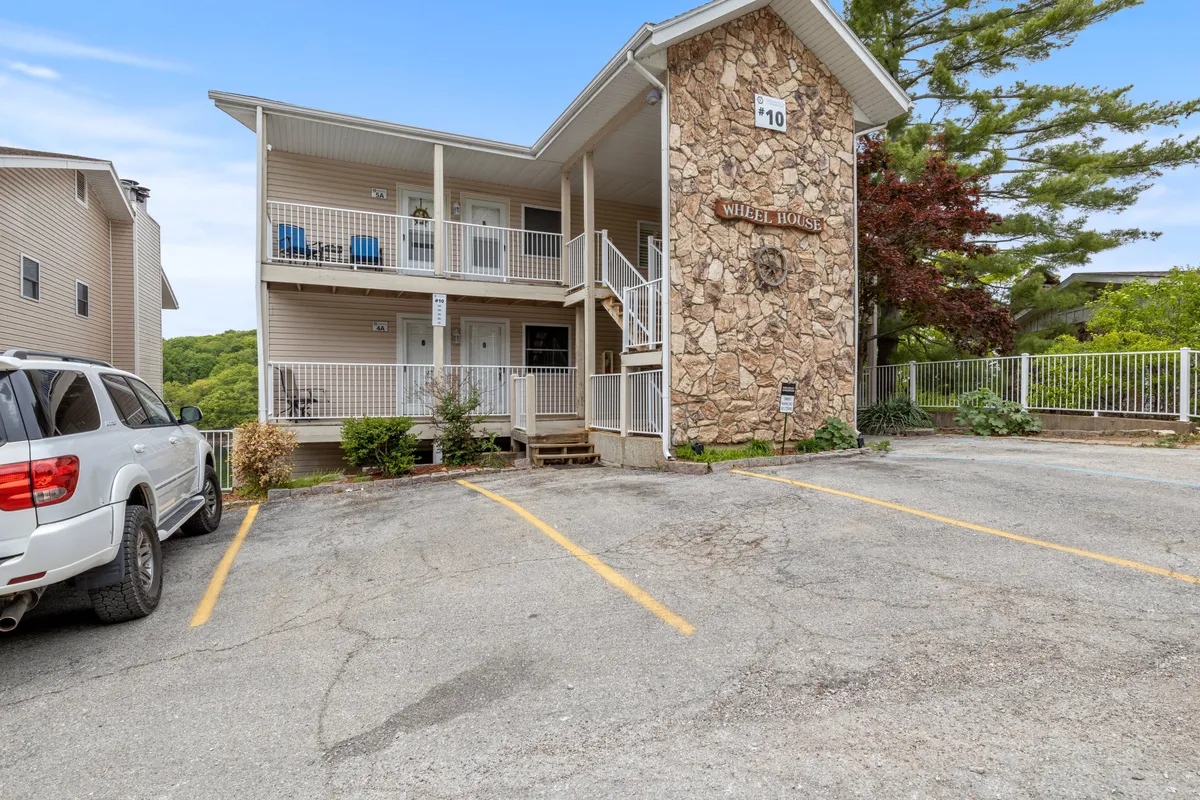 The exterior view of the condo building with stone facades, balconies, and a parking area. The balconies overlook natural surroundings, hinting at opportunities for morning coffee or evening gatherings with friends overlooking the lake.