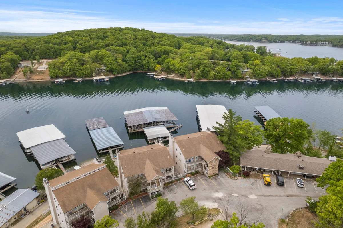 This exterior scene features a marina lined with boat docks, framed by abundant green trees and adjacent residential buildings. The area is bustling with possibilities for outdoor activity, including boating, fishing, water sports, and picnicking. The view emphasizes the direct access to the lake and nearby nature trails, reinforcing the outdoor recreation theme.